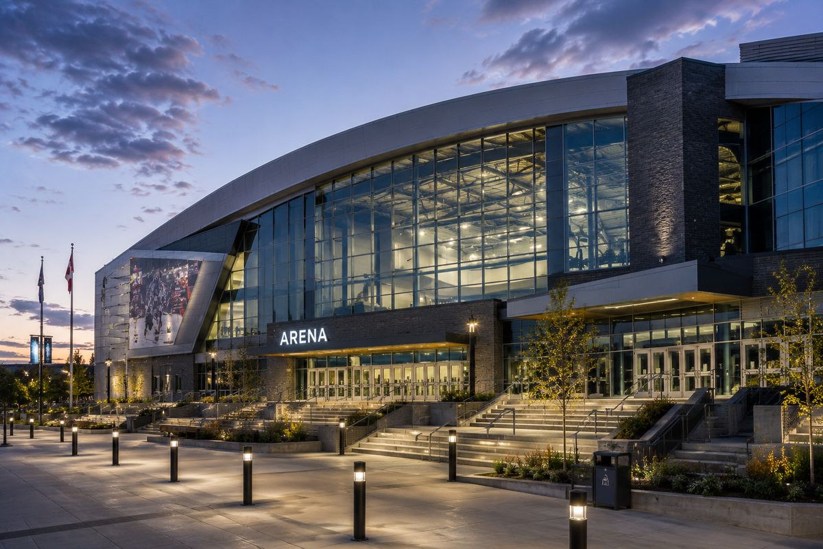 A modern arena at dusk with a curved glass frontage and lit entrance plaza