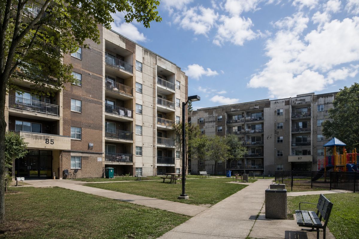Two mid-century public housing blocks in daylight with a shared green and playground
